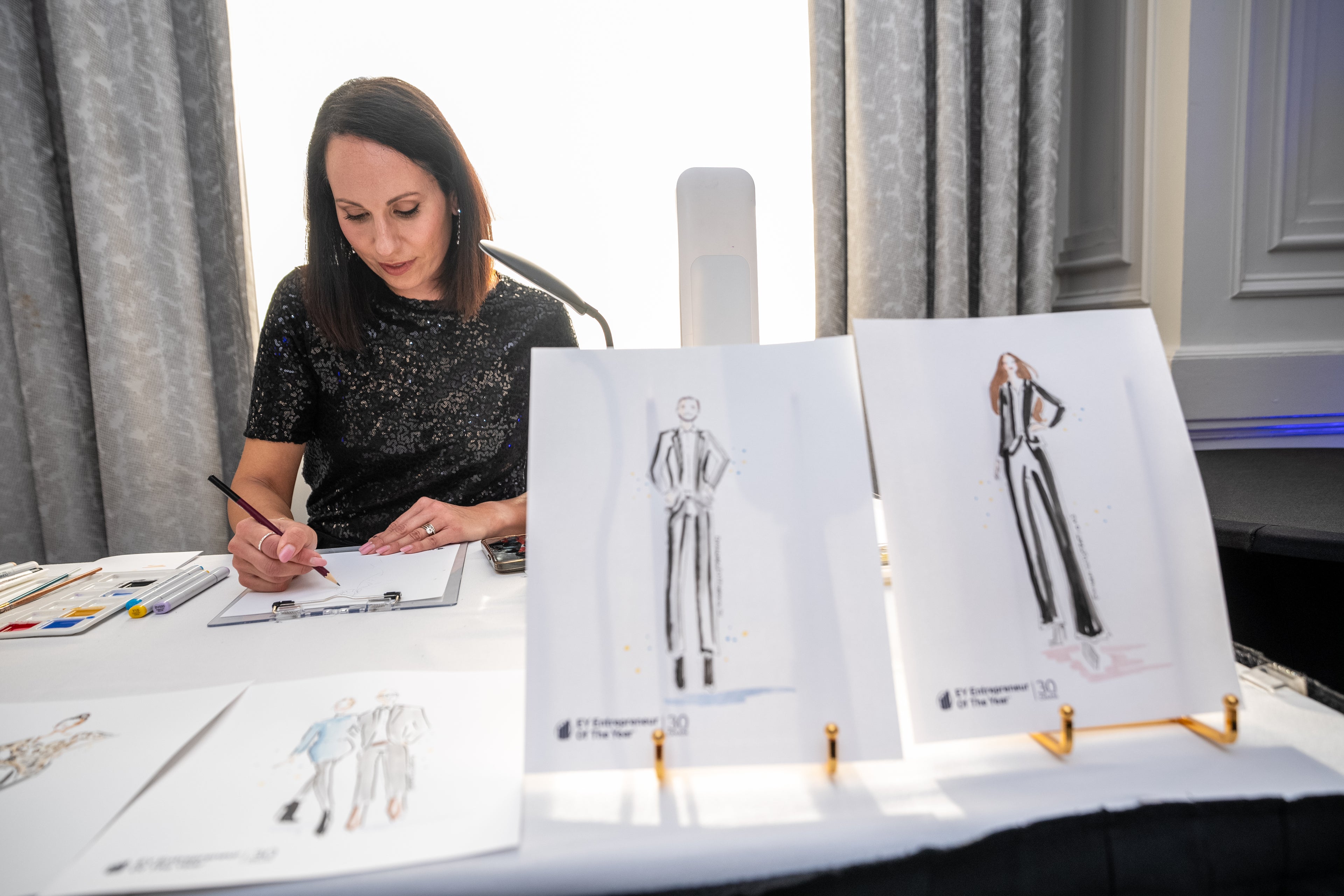Nina Maric working on fashion sketches with illustrations displayed on a table.