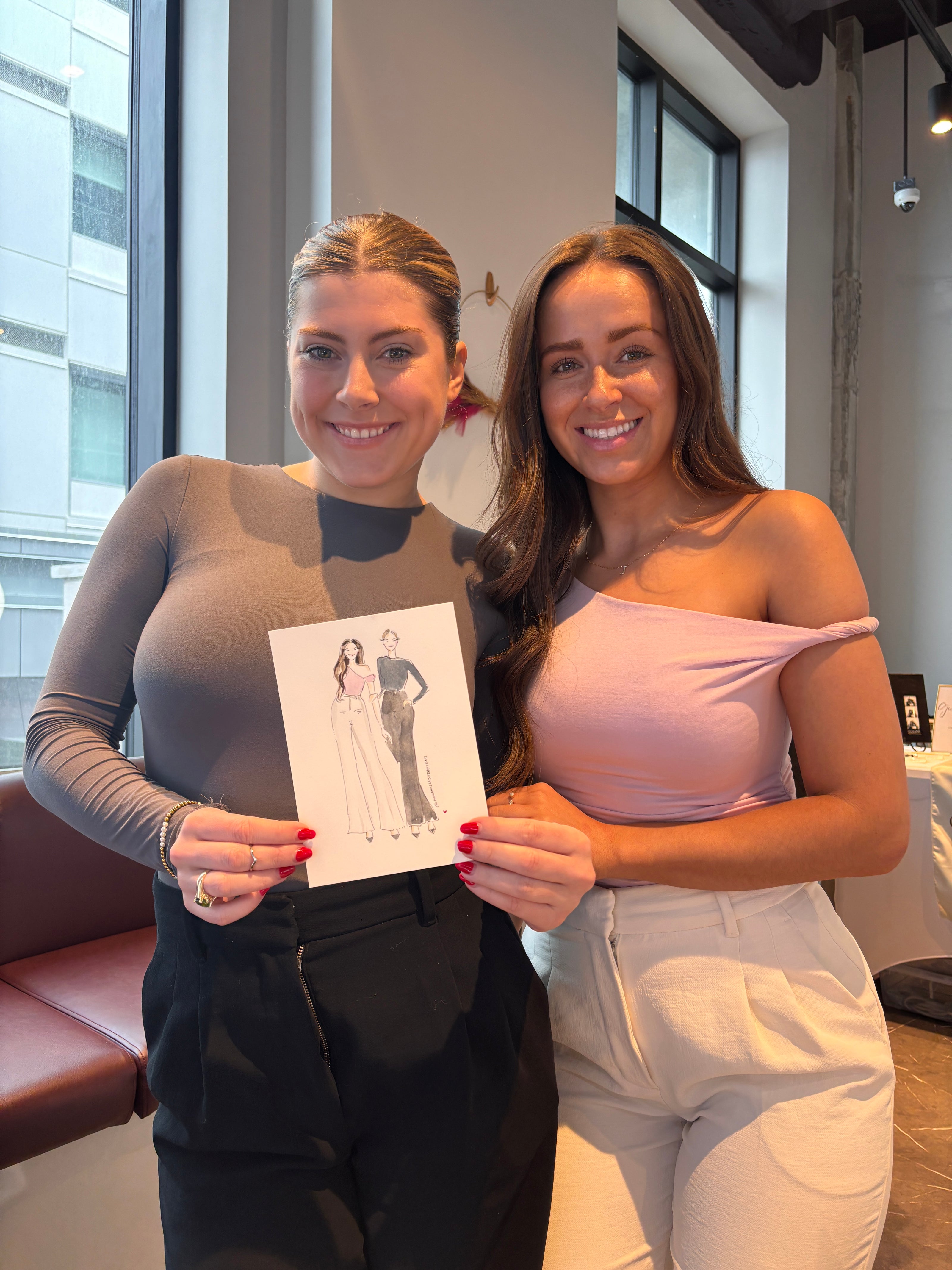 Two women standing next to each other, one holding a piece of paper with a design.