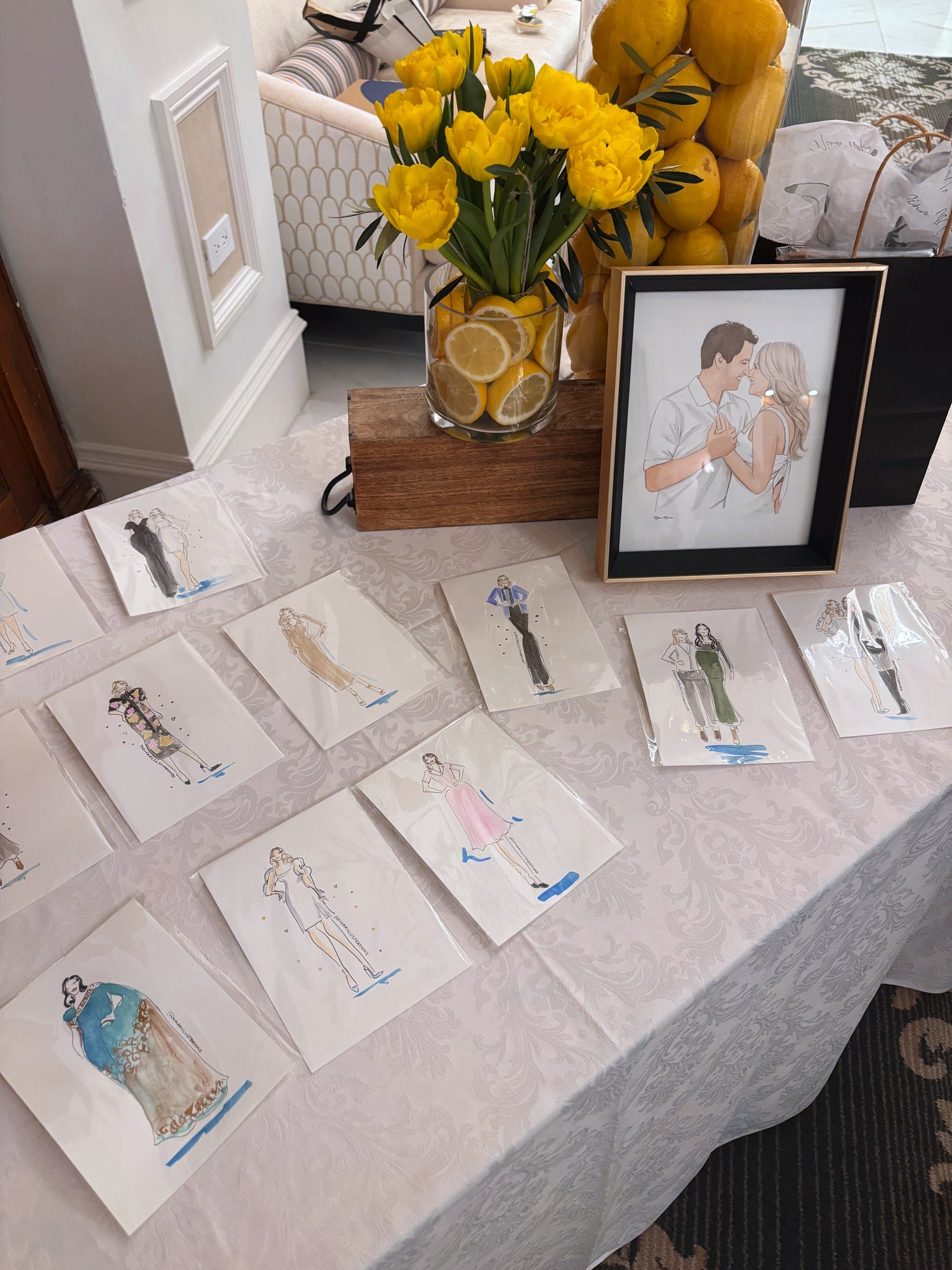 Table with illustrations, a vase of yellow tulips, and framed artwork.