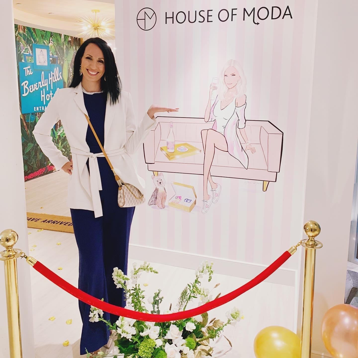 Nina Maric posing in front of a 'House of Moda' branded backdrop with a red velvet rope.
