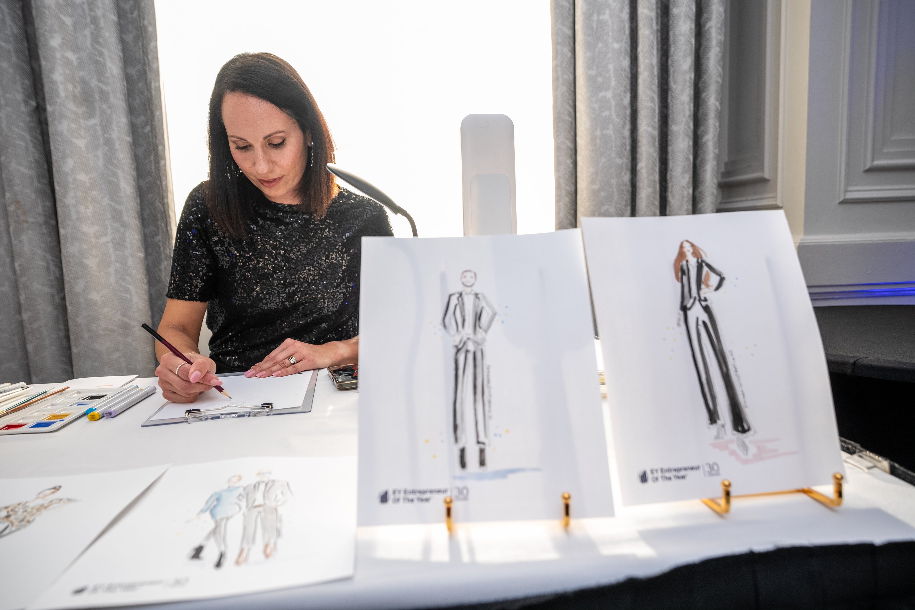 Nina Maric working on fashion sketches with illustrations displayed on a table.